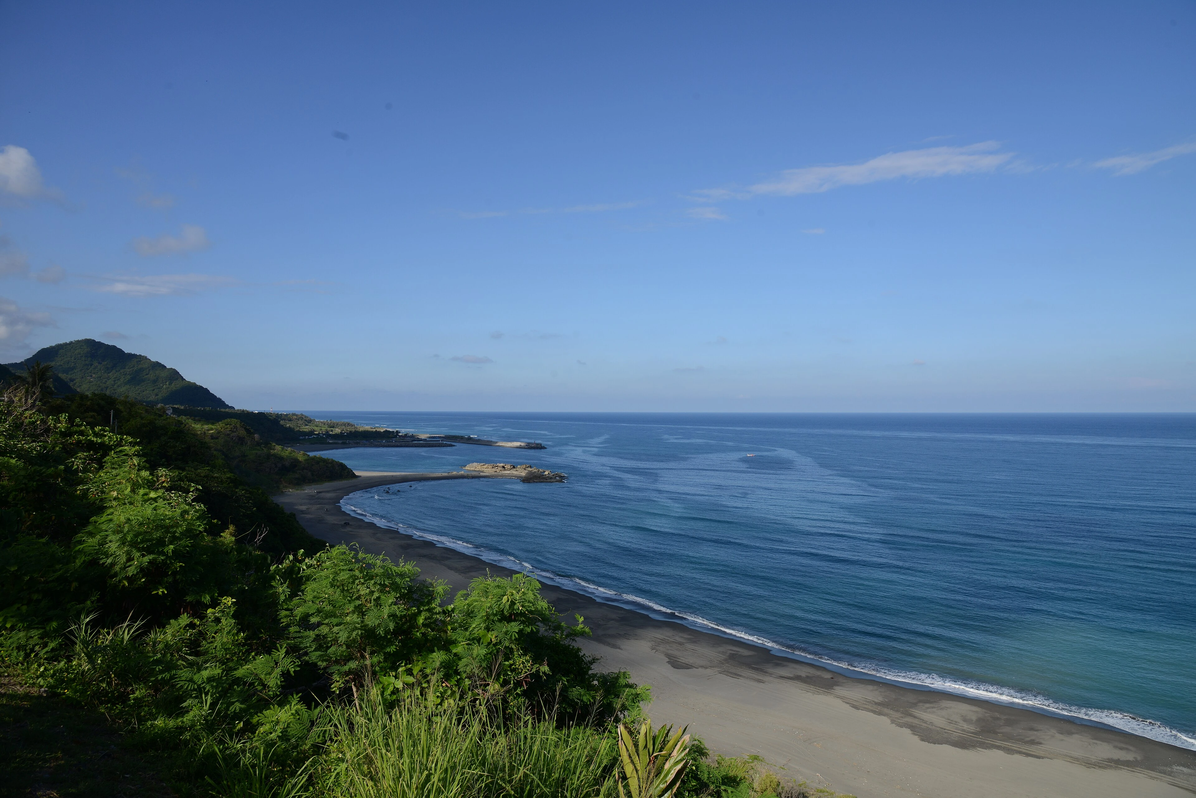 Donghe Township, on the eastern coast of Taitung, Taiwan. The Pacific opens wide here, and the waves arrive with weight, breaking long and full against the shore. The sound surrounds — the deep roll of water moving in, the heavy collapse of each break, the long hiss as it pulls back across the sand and stones. Stones turning in the backwash, a low clatter beneath the surge. The wind off the sea, steady and salt-heavy. No road, no voices. Just the ocean meeting the edge of the island, again and again, the cliffs of the coast holding the sound in close. The horizon is vast and uninterrupted. The Pacific keeps speaking into the morning, and there is nothing else to listen to.
