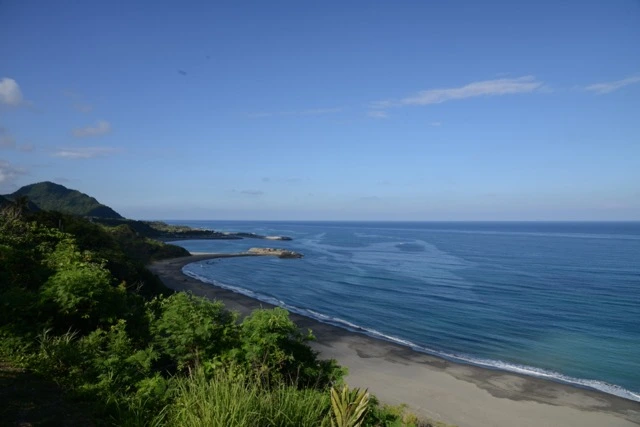 Donghe Township, on the eastern coast of Taitung, Taiwan. The Pacific opens wide here, and the waves arrive with weight, breaking long and full against the shore. The sound surrounds — the deep roll of water moving in, the heavy collapse of each break, the long hiss as it pulls back across the sand and stones. Stones turning in the backwash, a low clatter beneath the surge. The wind off the sea, steady and salt-heavy. No road, no voices. Just the ocean meeting the edge of the island, again and again, the cliffs of the coast holding the sound in close. The horizon is vast and uninterrupted. The Pacific keeps speaking into the morning, and there is nothing else to listen to.