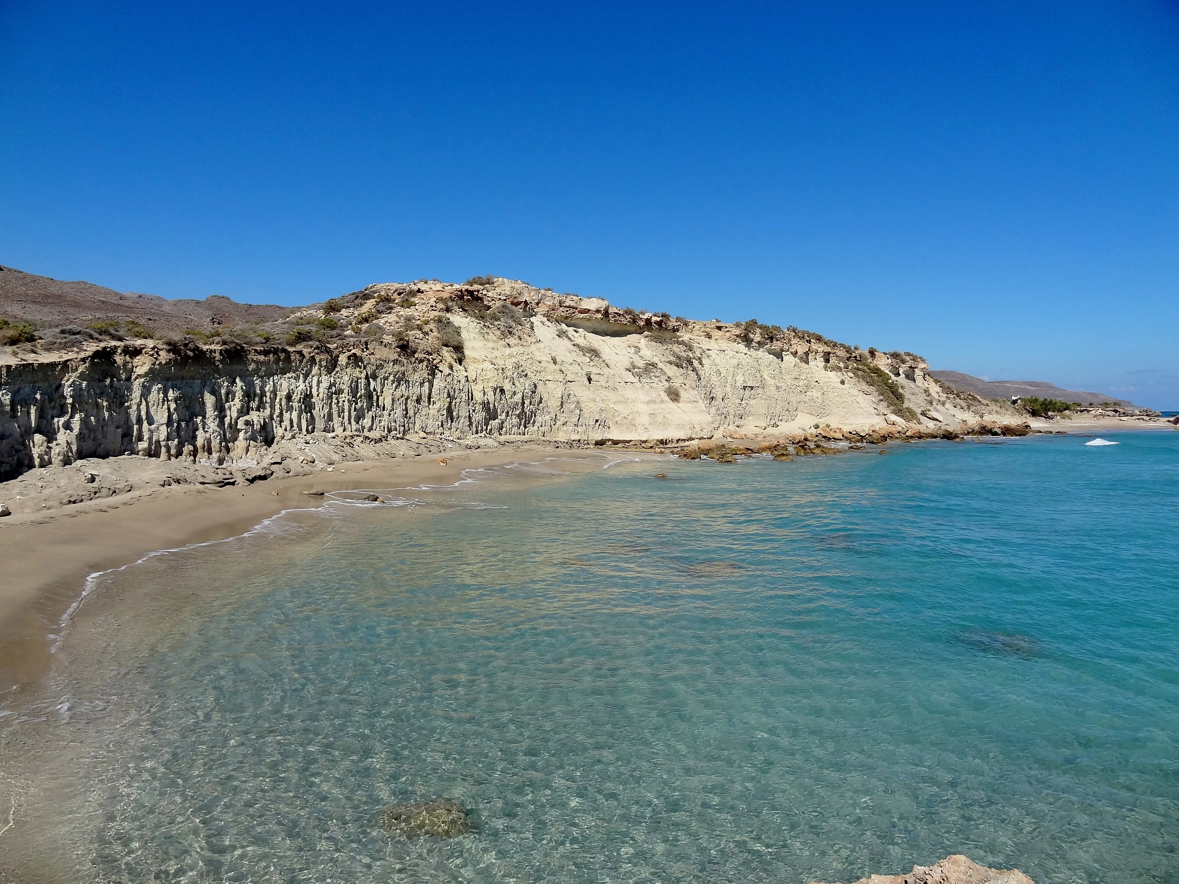 Xerokambos, on the eastern edge of Crete, where the island runs out of road and the Libyan Sea begins. Early morning, the light still pale and unhurried, the air carrying salt and the dry scent of thyme from the hills behind. The sea arrives in long, low pulses, breaking close to the shore and unfurling across the sand in thin sheets of white. The tide is on the turn, and the rhythm of the waves is quietly rewriting itself — a longer wait, then a closer break, then two arriving almost on top of each other, the sea momentarily forgetting its own count. Pebbles roll and click in the backwash, a small percussion underneath the larger breath of the water. Somewhere out beyond sight, a gull. The wind barely stirs. The horizon is empty. The Aegean and the Libyan trade something across this shore, again and again, while the morning slowly opens around it.